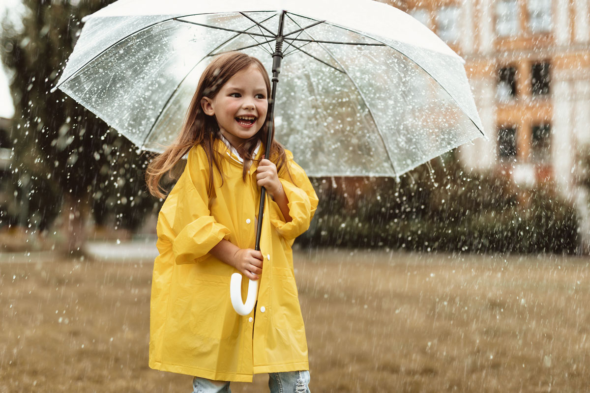 Une enfant porte un imperméable et tient un parapluie. Il pleut. 