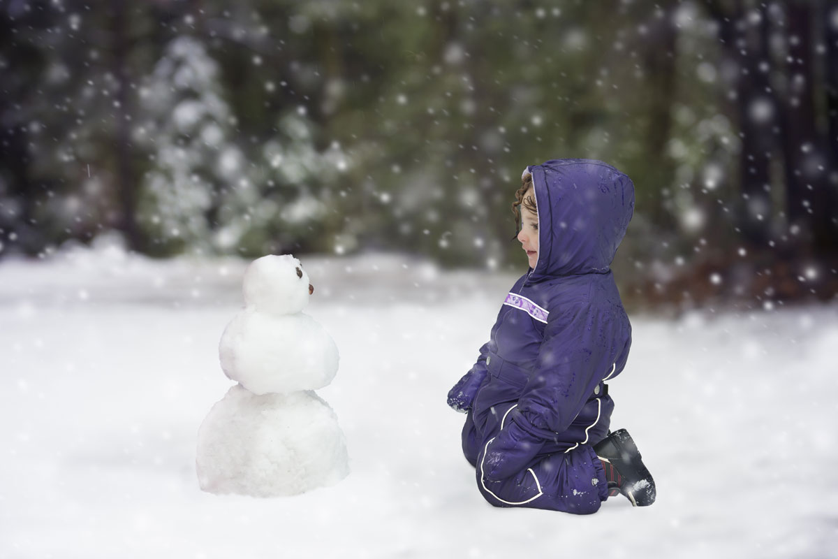 Un enfant qui fait un bonhomme de neige. Il porte un habit de neige. 