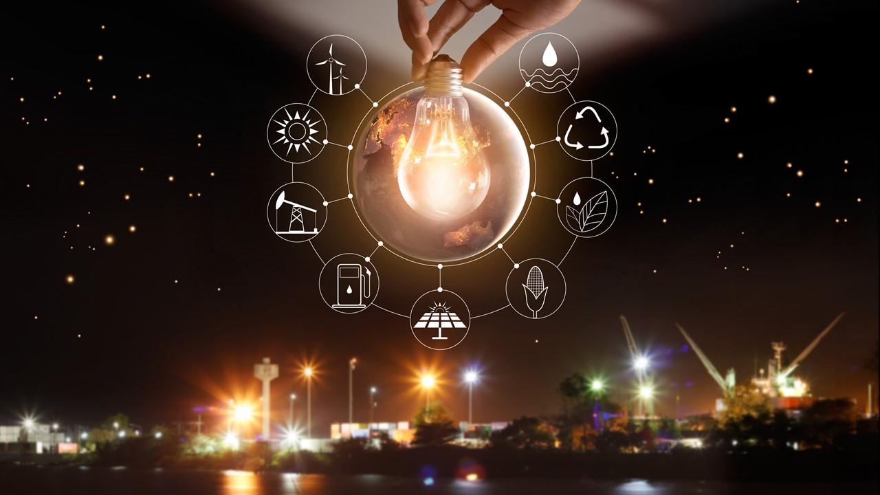 Montage-photo montrant une ville illuminée le soir. Au centre, on voit une ampoule allumée entourée de neuf icônes : éoliennes, soleil, foreuse de pétrole, distributeur d’essence, panneau solaire, blé d’Inde, eau et feuilles, symbole des produits recyclés, eau. 
