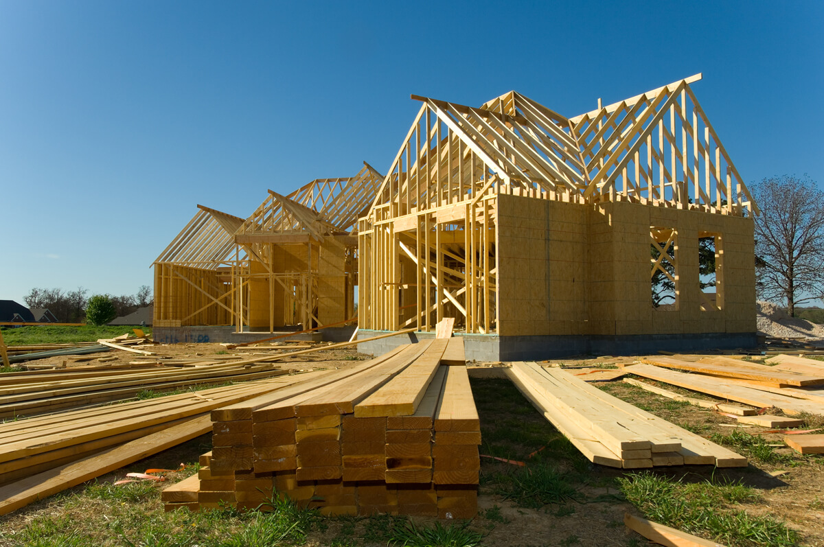 La charpente d’une maison en construction et des piles de planches de bois au sol 